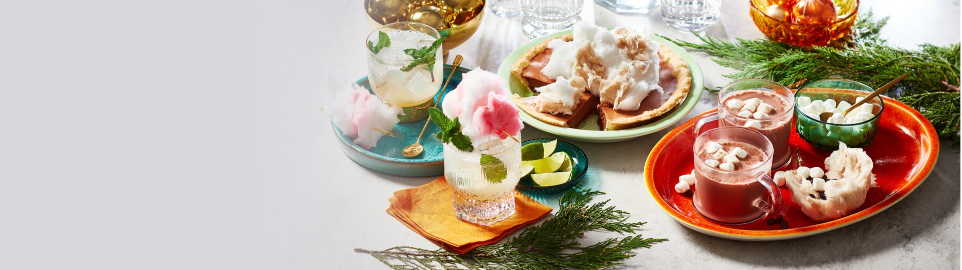 Marble table with three cotton candy-based treats: cotton candy hot chocolate, cotton-candy-topped cream pie and a zero proof cotton candy mojito