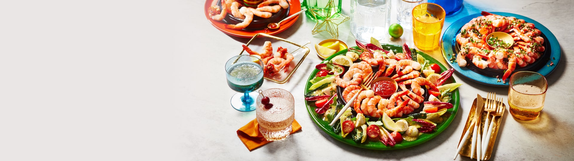 Marble table with three shrimp ring appetizers set out: shrimp ring with gremolata, shrimp ice ring wreath and a shrimp ring with romesco-style dipping sauce