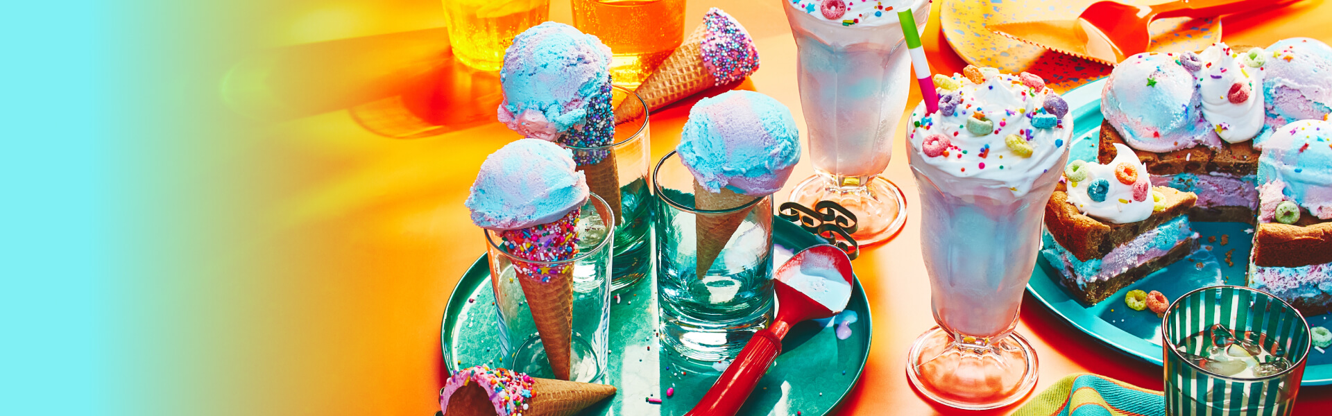 Unicorn twirl ice cream in sugar cones, in a milkshake, and ice cream cookie cake on an orange back drop.