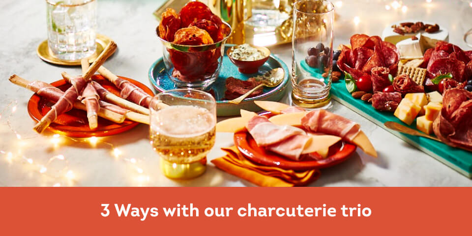 Marble table with twinkle lights, a charcuterie board, plate of salami chips, and prosciutto-wrapped melon and breadsticks.