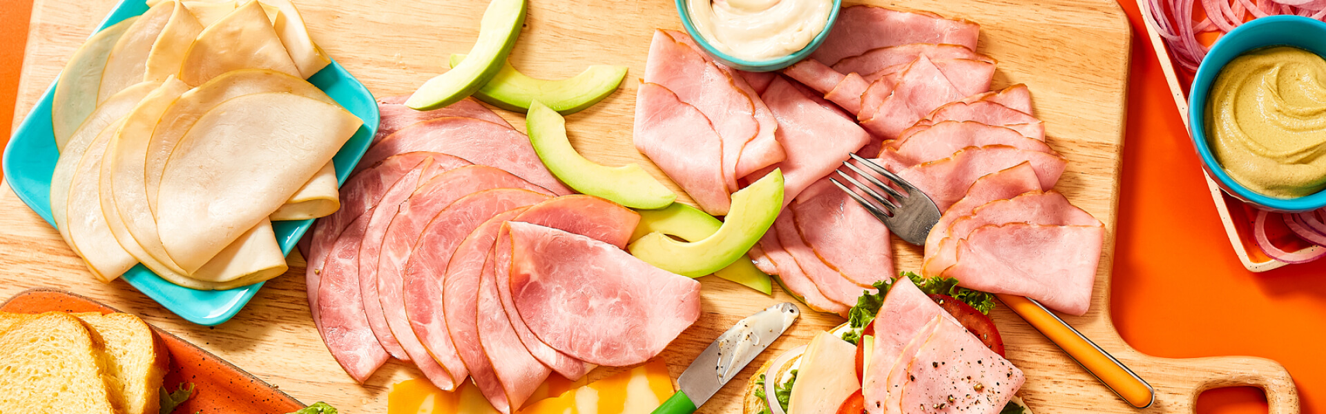 Overhead shot of all natural deli-meats on cutting board with sliced avocados