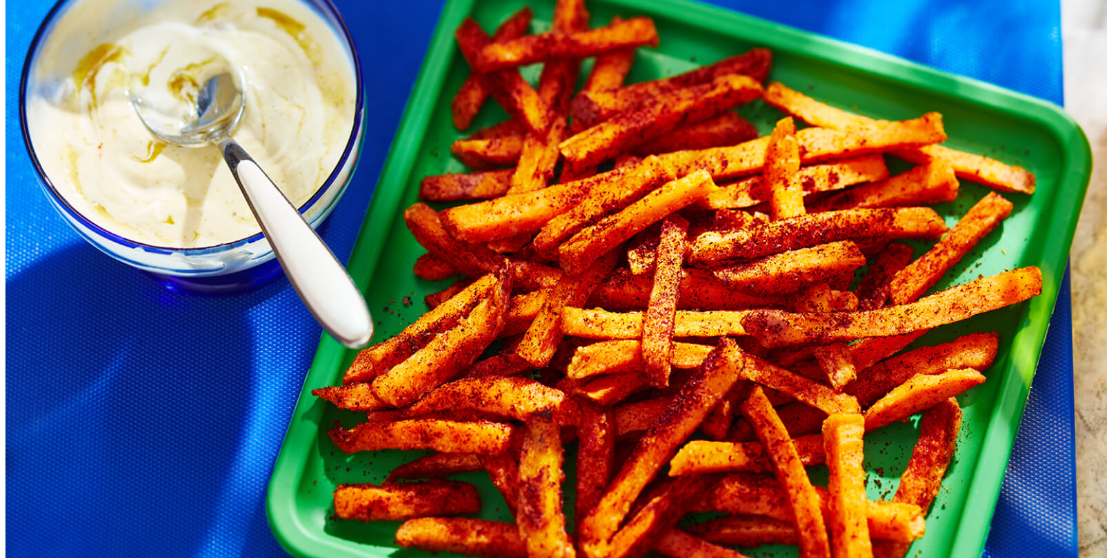 Frites de patates douces sur une assiette verte avec un côté de trempette extra épicée dans un bol.