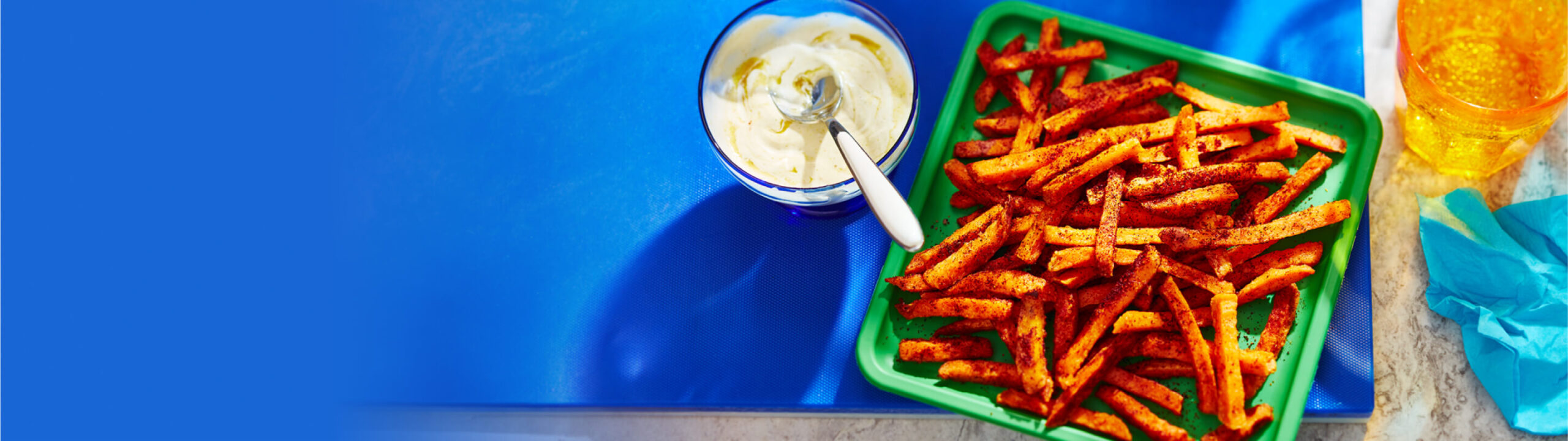 Frites de patates douces sur une assiette verte avec un côté de trempette extra épicée dans un bol.