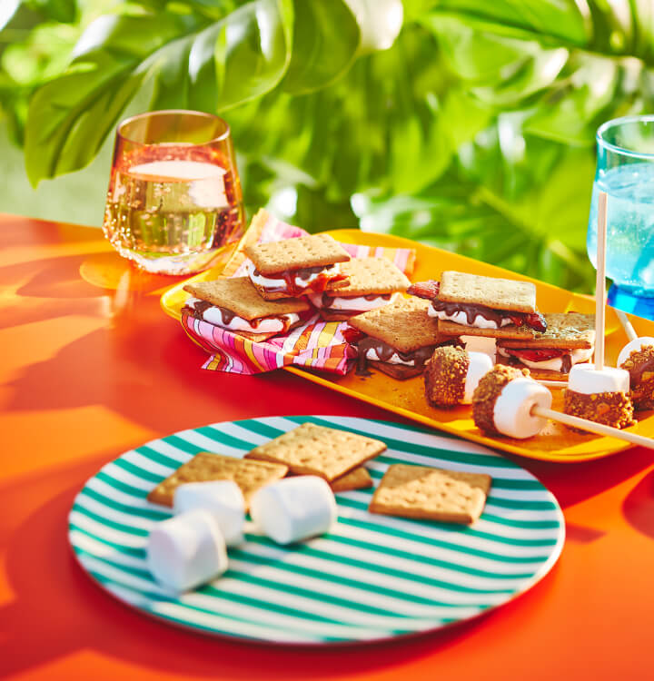 table orange avec plateaux de s'mores - s'mores au caramel, s'mores au bacon et s'mores et sucettes glacées à la guimauve